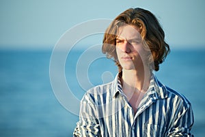 Portrait of serious young teenager boy at sea sunset
