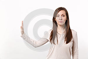 Portrait of serious young woman in light clothes showing stop gesture with palm aside isolated on white wall background