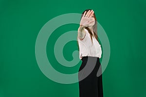 Portrait of a serious young woman standing with outstretched hand showing stop gesture isolated over green background