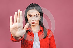 Portrait of a serious young woman standing with outstretched hand showing stop gesture sign isolated over pink background