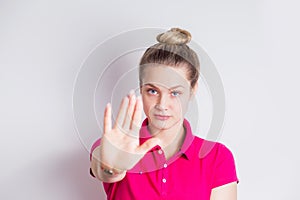 Portrait of a serious young womanin in pink dress standing with outstretched hand showing stop gesture over white background. Body