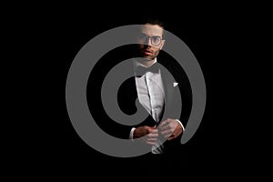 Portrait of sexy arabic man with glasses adjusting and buttoning black tuxedo