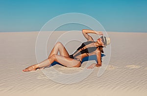 Portrait of sexy beautiful tanned model woman posing in fashion black swimwear bikini, fedora hat and sunglasses sand desert beach