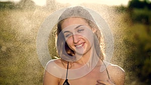 Portrait of a sexy, beautiful young blonde girl, under a light summer rain, in the sun rays, on a green meadow. The girl