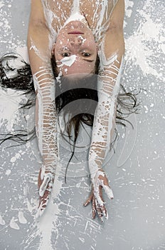 Portrait of a sexy brunette woman with raising arms painted with white paint on the studio floor, creative expressive abstract