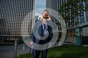 Portrait sexy business man using smartphone near modern building outdoor. Successful businessman walking in suit at