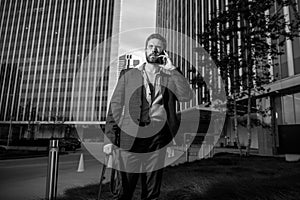 Portrait sexy business man using smartphone near modern building outdoor. Successful businessman walking in suit at