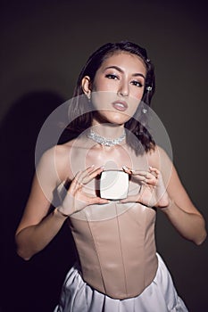 portrait of a sexy fashionable makeup artist girl in a white skirt shows a white square box of powder standing in the