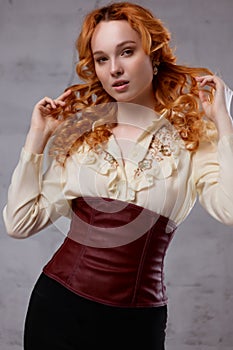 Portrait of a sexy red-haired woman in a skirt, blouse and corset.