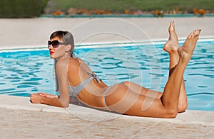 Portrait of sexy tanned slim model woman in sunglasses and striped retro bikini have relax and enjoy in swimming pool. Hot summer