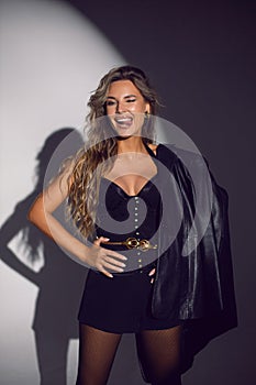 portrait of a sexy woman in a black corset, shorts and boots stands in the studio on a white cyclorama with a light spot