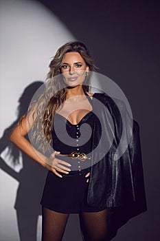 portrait of a sexy woman in a black corset, shorts and boots stands in the studio on a white cyclorama with a light spot