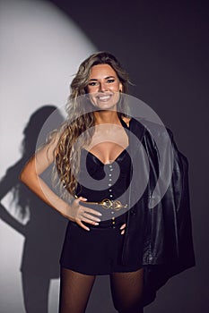 portrait of a sexy woman in a black corset, shorts and boots stands in the studio on a white cyclorama with a light spot