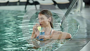 Portrait of sexy woman drinking cocktail at pool. Wet girl resting with cocktail