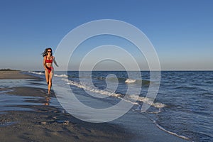 Portrait of sexy woman in red swimsuit. Girl run on empty sea shore before sunset