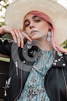 Portrait sexy young beautiful woman with pink hair in fashionable straw hat in stylish black leather jacket in blue dress near