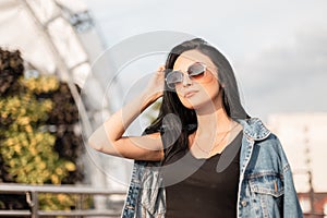 Portrait of a sexy young brunette woman in trendy sunglasses in stylish clothes outdoors. Beautiful hipster girl