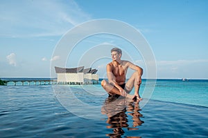 Portrait of sexy young handsome man in infinity swimming pool at the tropical island luxury resort