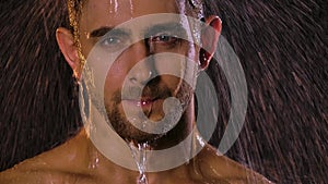 Portrait of a sexy young man under shower jets who looks erotically into the camera. Water flows down his face creating