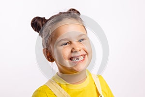 Portrait of shining little kid showing missing front baby tooth and smiling looking away in yellow t-shirt on white