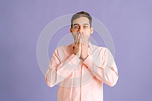 Portrait of shocked amazed excited young man standing covering mouth with hands looking camera on isolated purple