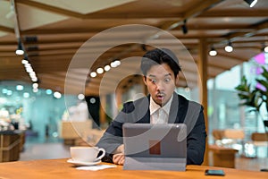 Portrait of shocked Asian businessman in coffee shop using digital tablet computer