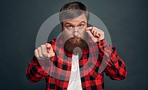 Portrait of a shocked bearded man in eyeglasses looking at camera isolated over grey background