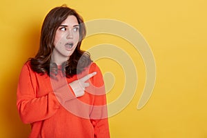 Portrait of shocked caucasian female with pleasant appearance indicates aside at blank yellow wall  has surprised and astonished