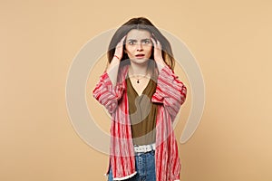 Portrait of shocked concerned young woman in casual clothes putting hands on head isolated on pastel beige wall