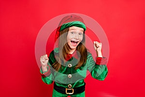 Portrait of shocked elf kid in green hat cap with long red head hairstyle raising her fists celbrate newyear party