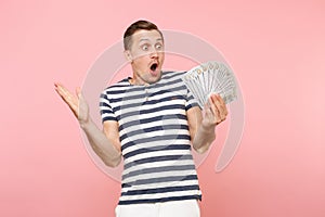 Portrait of shocked excited young man in striped t-shirt holding bundle lots of dollars, cash money, ardor gesture on