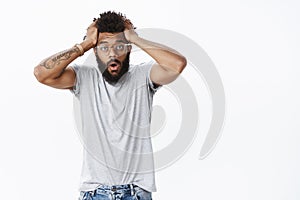 Portrait of shocked freak-out african american male in glasses grabbing hair open mouth folding lips and raising