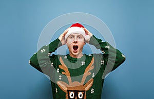 Portrait of shocked guy in santa claus hat and green warm sweater, startled by surprise, looking into camera with mouth open.