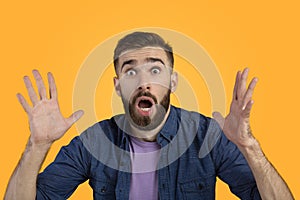 Portrait of shocked man with open mouth looking at camera in amazement, making surprised gesture over orange background