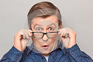 Portrait of shocked man peering over glasses at something unbelievable