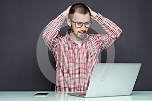 Portrait of shocked man sitting at the table with laptop on gray background