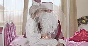 Portrait of shocked Santa Claus listening to wishes of pretty Caucasian girl. Cute child whispering on Santa`s ear and