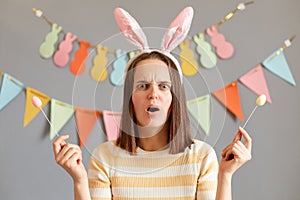 Portrait of shocked scared surprised woman wearing striped shirt celebrating easter isolated over gray background, being surprised