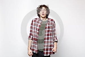 Portrait of shocked scared young man in casual clothes looking camera, keeping mouth open isolated on white wall