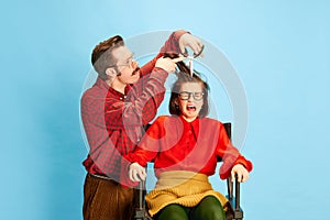 Portrait with shocked, screaming woman and crazy barber, hairdresser doing new haircut over blue color studio background