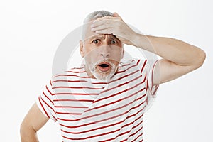 Portrait of shocked speechless concerned old man punching forehead with palm with troubled look open mouth and looking