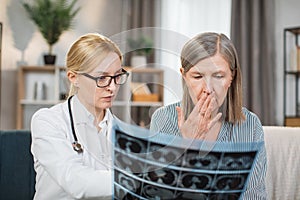 Portrait of shocked surprised elderly gray-haired lady patient, sitting at home and listening to her doctor blond woman