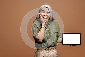 Portrait of the shocked surprised woman holding tablet and looking at the camera with big astonished eyes. Indoor studio