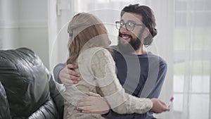 Portrait of shocked unhappy Caucasian man in eyeglasses embracing his wife. Woman showing affirmative pregnancy test and