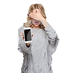 Portrait of shocked woman covering her eyes with hand showing mobile phone blank screen isolated over white. Shocking news.