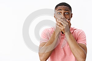 Portrait of shocked worried and concerned insecure african american young man holding hands on mouth gasping feeling