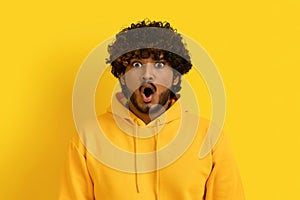 Portrait of shocked young indian guy on yellow background