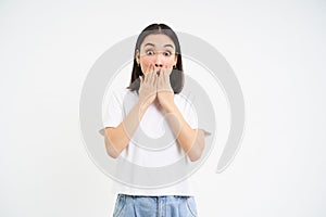 Portrait of shocked young korean woman, gasps, covers mouth with surprised face, isolated on white background