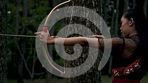 Portrait shoot of female shooting an arrow from the bow in the forest