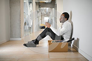 Portrait shot of African American sad businessman in suit and tie sitting with box of stuff. Male office worker lost job